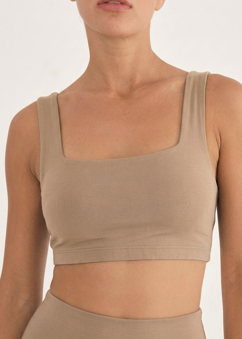 A close-up of a model wearing a beige square-neck crop top and matching high-waisted bottoms against a plain light background.